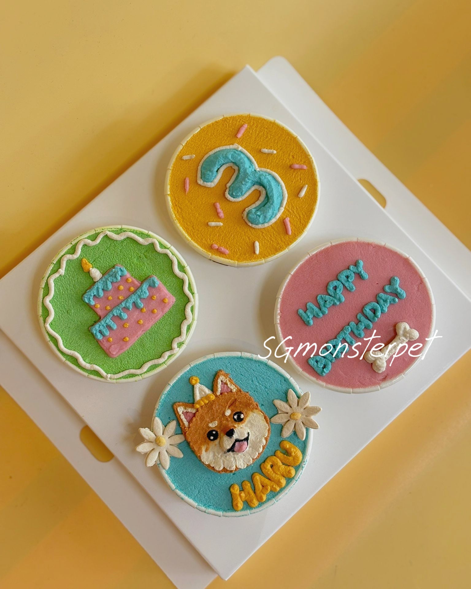 Four colorful cupcakes with decorative icing on a white tray against a yellow background.
