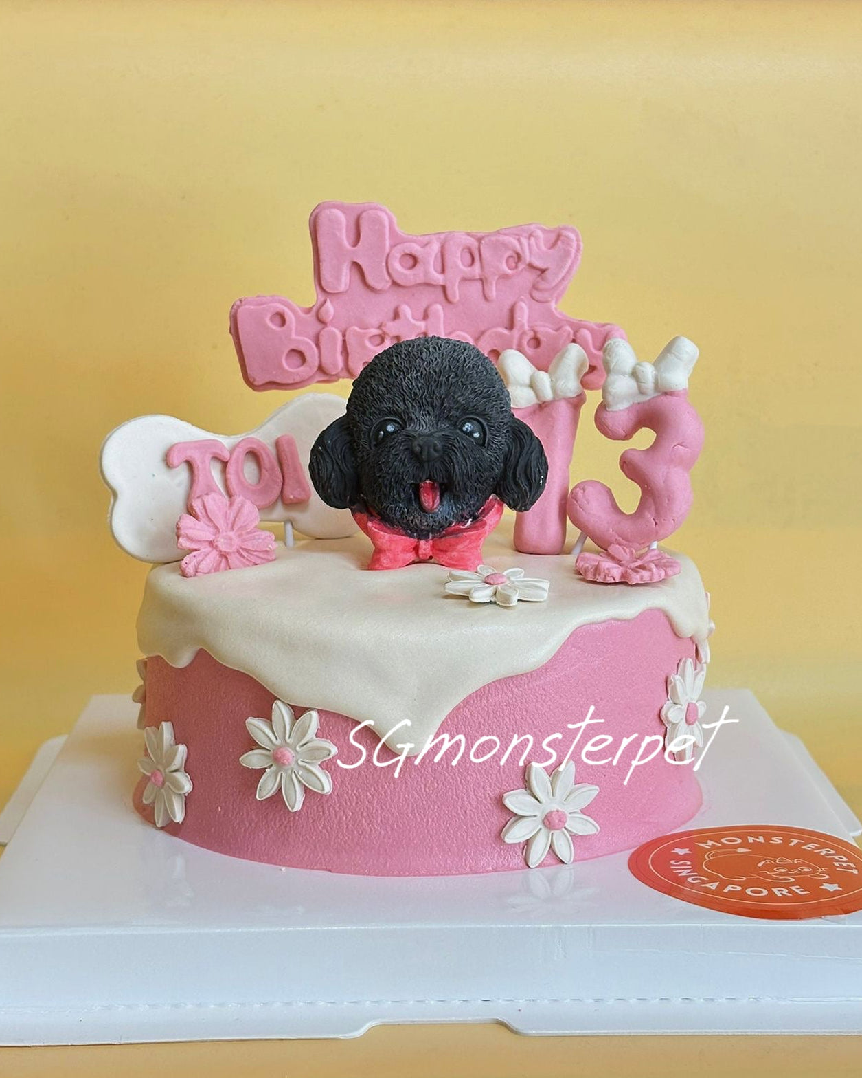 Pink birthday cake with a black dog figurine and 'Happy Birthday' topper on a yellow background.
