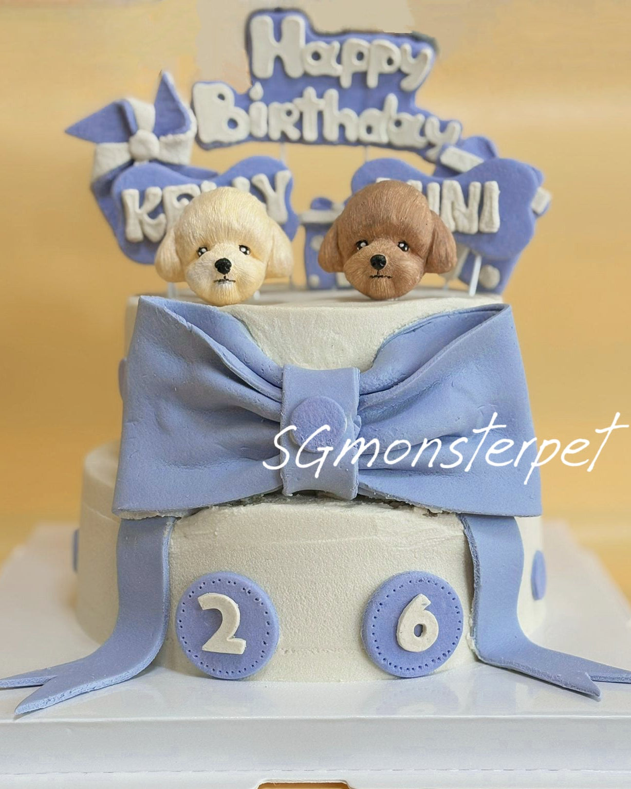 Two-tier birthday pet cake with fondant dogs, blue ribbon, and 'Happy Birthday' topper